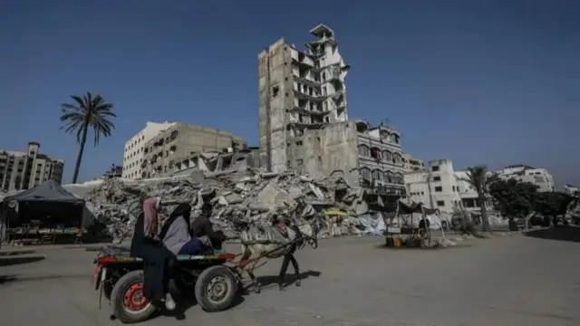 Displaced Palestinians ride on a carriage pulled by a horse on a road in Gaza City surrounded by ruined buildings