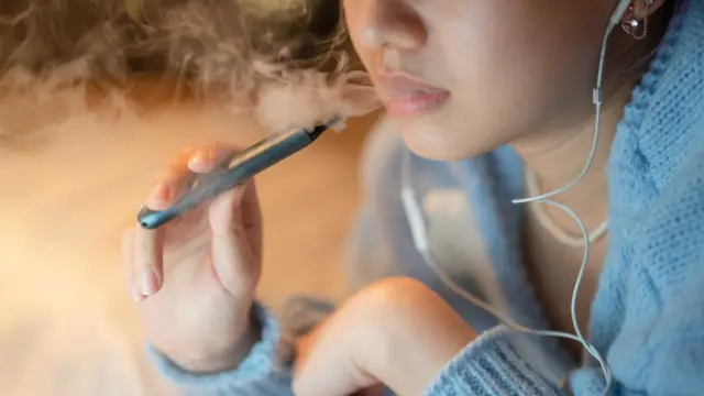 Stock picture of the bottom half of a young woman's as she breathes out lots of smoke from a vape she holds near her mouth