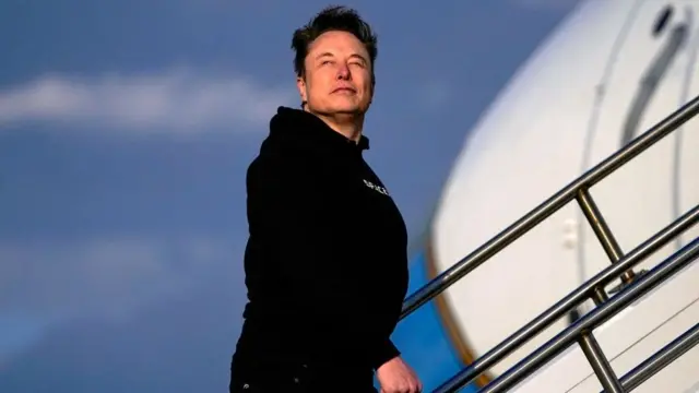 Musk walking up the steps of a plane looking out into the distance