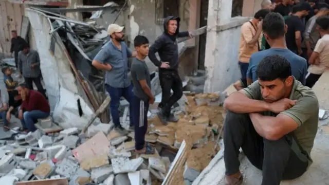 A man sits as Palestinians gather at the site of an Israeli strike on a house in Gaza.
