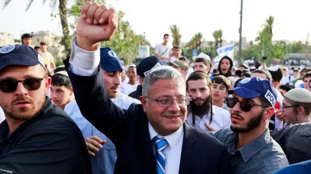 Itamar Ben-Gvir walks to visit the Damascus Gate to Jerusalem's Old City, as Israelis mark Jerusalem Day, in Jerusalem. He has two police officers next to him and several orthodox Jewish men standing behind him.