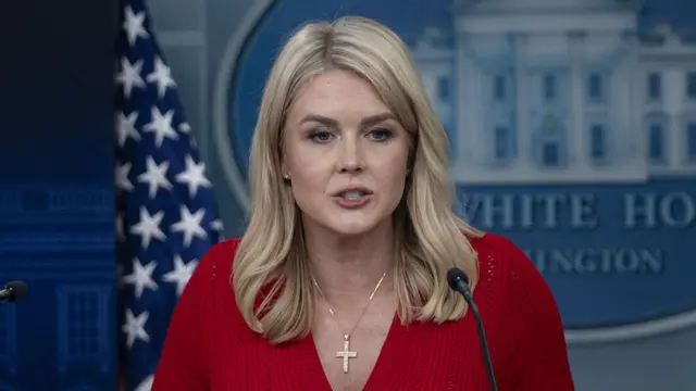 Karoline Leavitt in red crochet top with short sleeves and golden cross chain around her neck delivers daily press briefing inside the White House