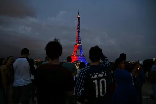 Crowds gather near the illuminated Eiffel Tower