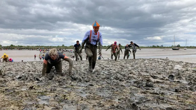 Someone crawling through the mud, while another participant walks near them,