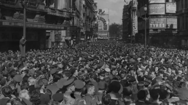 Soldiers and civilians assembled in Piccadilly Circus to mark VJ Day, Leicester Square's west side is visible in the far distance