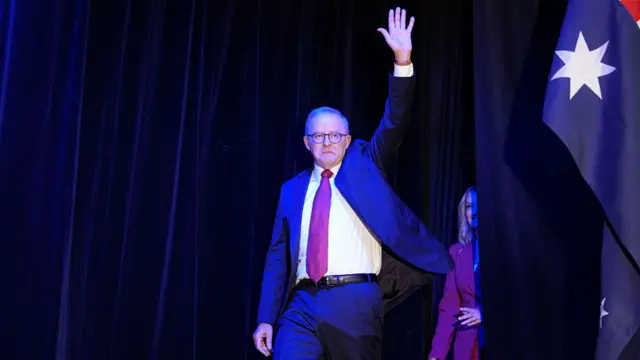 Anthony Albanese walking on stage and raising his hand