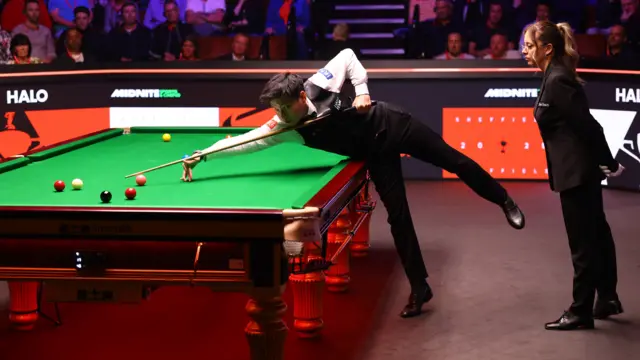 Zhao Xintong plays a shot in the World Snooker Championship final as referee Desislava Bozhilova watches on