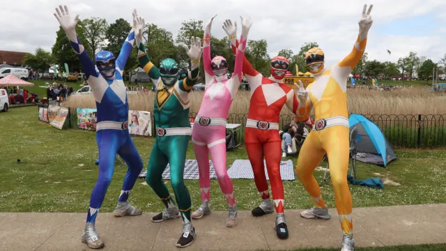 Five people dressed in Power Rangers outfits with their hands in the air