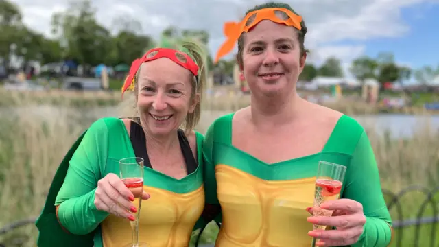 Lauren Scotcher and Alison are dressed in green teenage mutant ninja turtles costumes. they are holding glasses of prosecco.