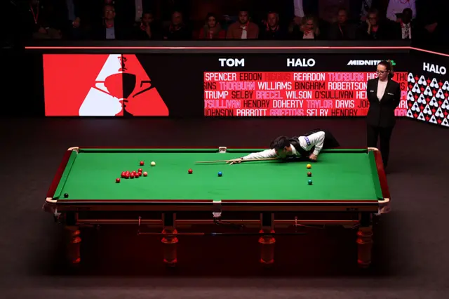 Zhao Xintong plays a shot with a list of previous world champions in the background