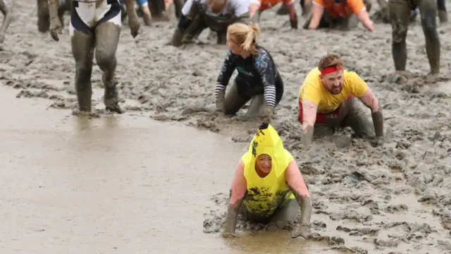A person dressed as a banana crawls through the mud