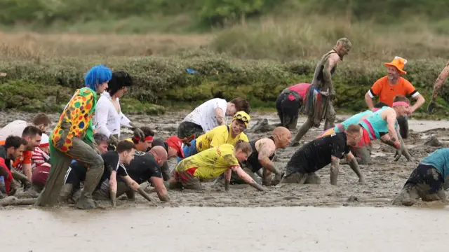 People in colourful costumes crawl through a muddy riverbank