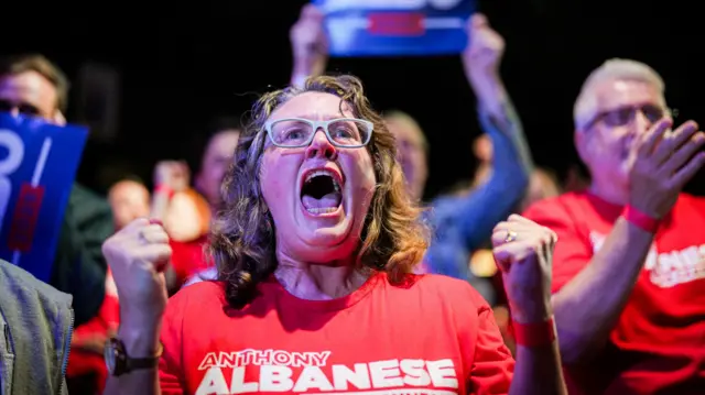 A woman opens her mouth wide in a cheer as she wears a shirt that reads "Anthony Albanese".