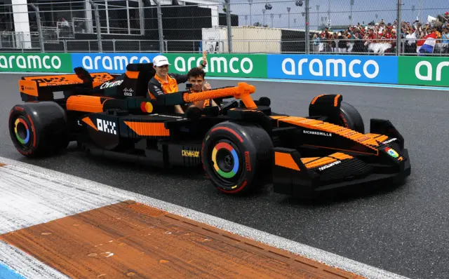 Lando Norris and Oscar Piastri wave as they are sat in a McLaren made up of Lego bricks at the Miami Grand Prix