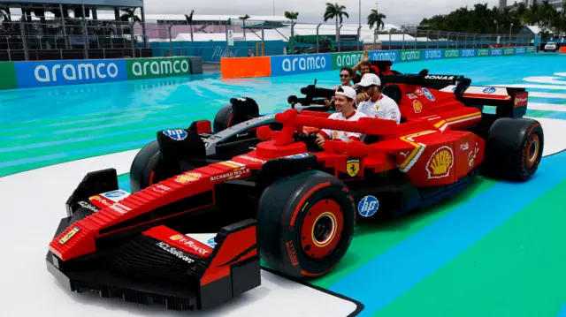 Lewis Hamilton and Charles Leclerc sat in a Ferrari made up of Lego bricks, with George Russell in a Mercedes made of Lego behind them