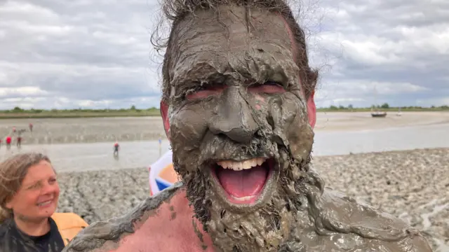 Joel Hicks has a face full of mud. it's stuck in his beard and hair and on his teeth.