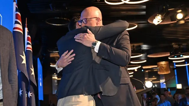 Peter Dutton embraces his son in a tight hug with Australian flags and a crowd behind him at his election watch party.