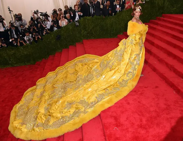 Rihanna wearing a yellow fur dress with a metre's long trail behind her on the red carpet at the Met.