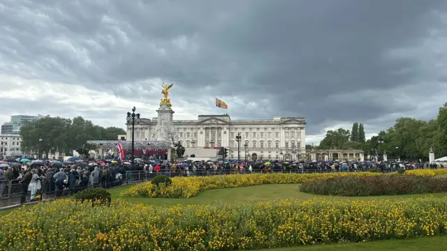 Buckingham Palace with a view of crowds wearing hoods and holding umbrellas