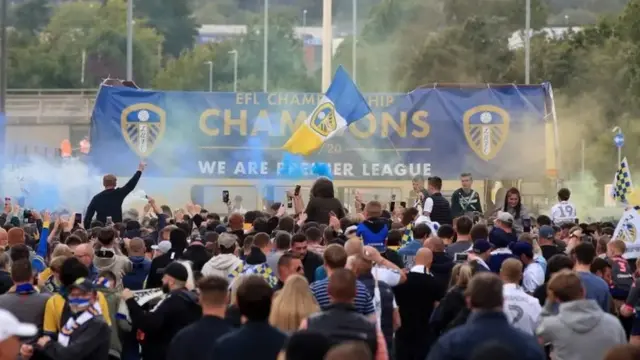 Open top bus with banner on, lots of fans in the foreground