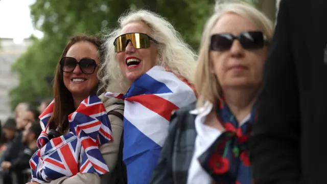 Two women among crowd look on smiling while draped in UK flags