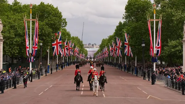 Members of the armed forces on horseback make their way down the Mall, which is lined with crowds and Union Jacks