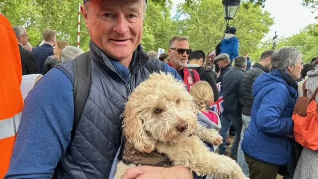 A man in the crowd holds a dog - many other onlookers can be seen behind