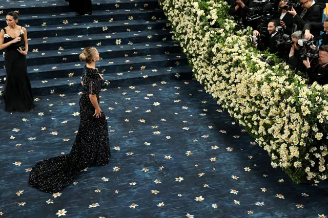 Actress Sydney Sweeney stands on the blue carpet of this year's Met Gala, which is adorned with daffodils.