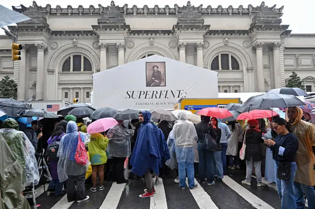 Spectators brave the rain in ponchos and umbrellas to gawk outside the Met Gala red carpet.