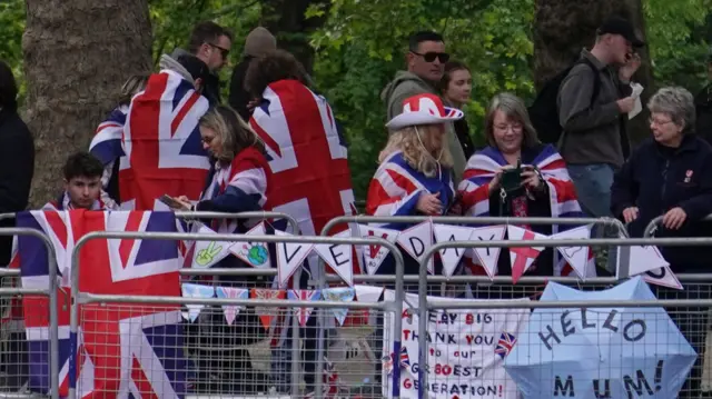 People wearing UK flags over their shoulders and preparing decorations while standing behind metal barriers