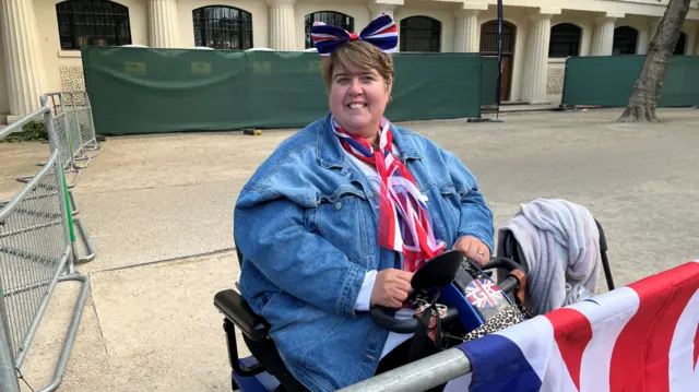 A lady seated is wearing a headband and a scarf featuring the Union Jack - she smiles at the camera
