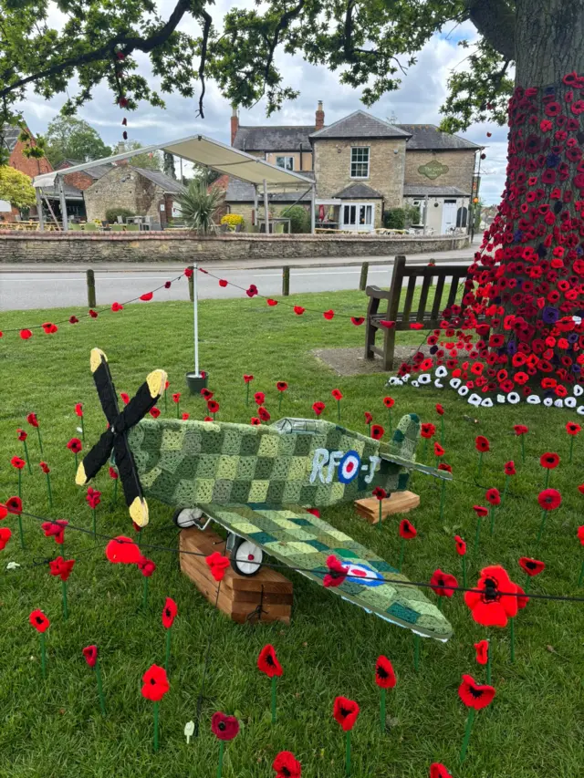 A yarn military plane on the grass surrounded by woollen poppies