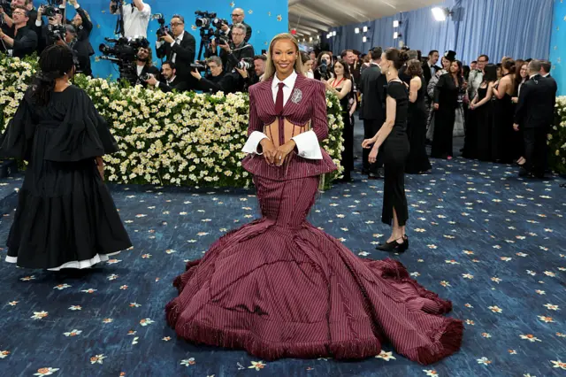 Savannah James wearing a stripped burgundy suit slash ball gown at the base.