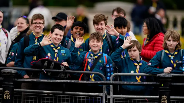 Scouts wave to the cameras from behind metal barriers