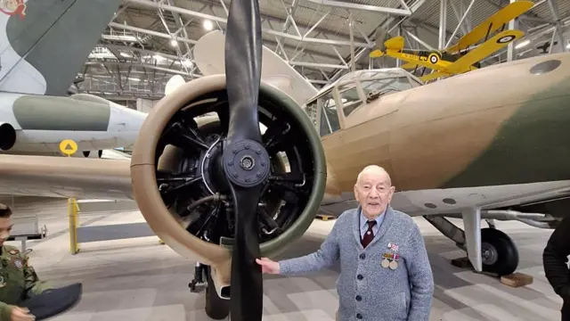Norman Brown stands holding the propeller of a plane - he wears medals on the left side of his chest