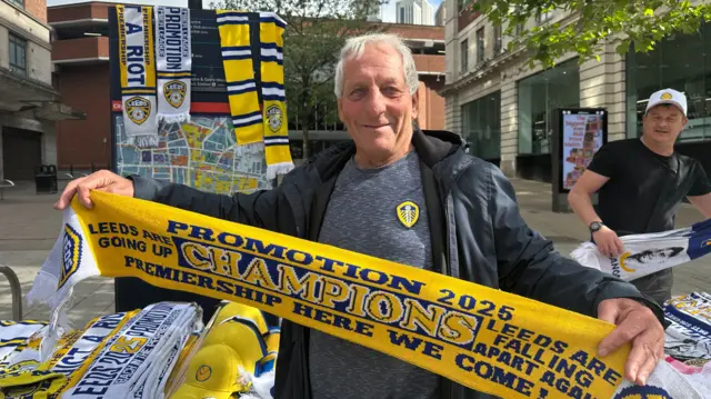 Man with Leeds T-shirt on holding out a Leeds scarf