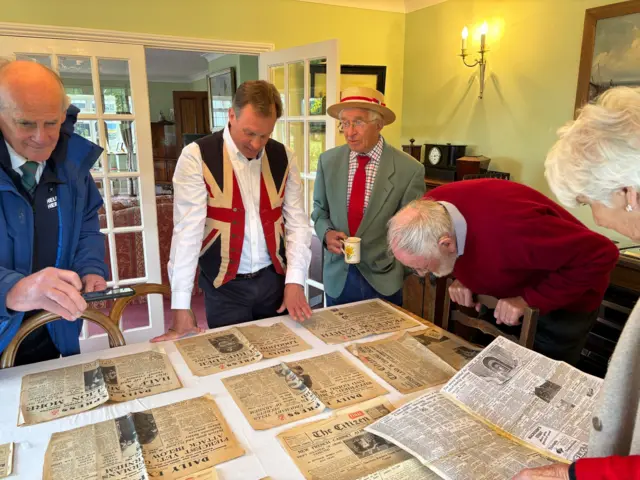 People looking at old newspapers spread out on a table