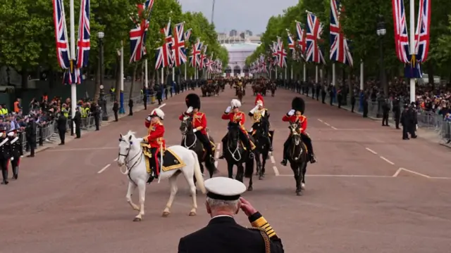 King Charles, seen from behind, salutes, as the Mall stretches out in front of him, as the procession moves along- including members of the armed forces on horseback