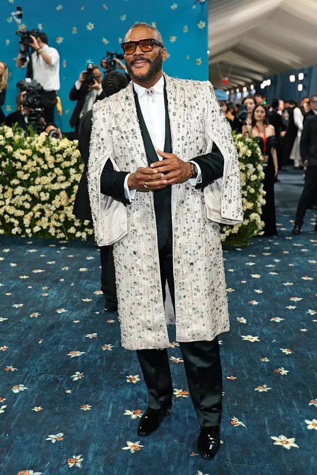 Tyler Perry wearing a black tux over white shirt. On top of that is a white bejewelled overcoat.