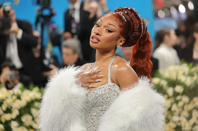 Megan Thee Stallion wearing a silver dress with fur on her arms and red die in her hair