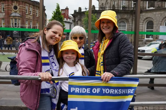 Three women and a young girl wearing Leeds United scarves and hats smile for a photo.