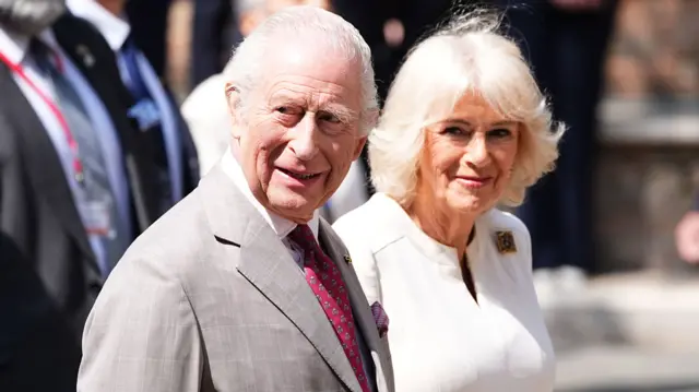King Charles and Queen Camilla look to the side of the camera and smile
