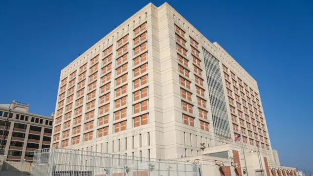 An outside image of Metropolitan Detention Centre in Brooklyn. The tall cube-shaped building is beige in colour.