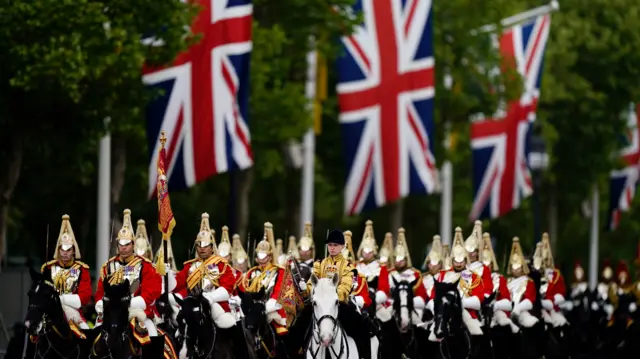 Members of the Household Cavalry Mounted Regiment progress along the Mall with union jacks hanging by the trees