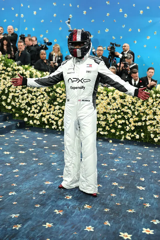 Damon Idris is dressed in an all white Formula One race gear and a sequenced helmet