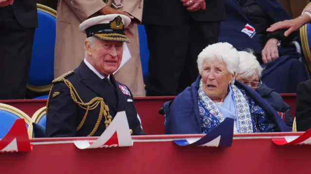 King Charles sits next to woman in stands