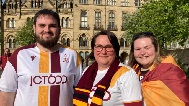 Kieran Swords, Julie Swords and Jess Swords wearing Bradford City tops. Julie is wearing a Bradford scarf and Jess is wearing a flag around her shoulders.
