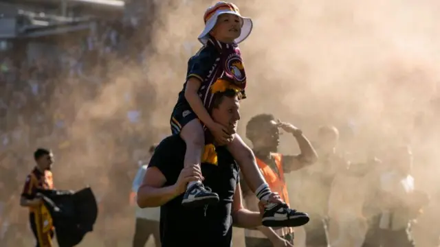 A man holds his son his shoulders as they celebrate among smoke