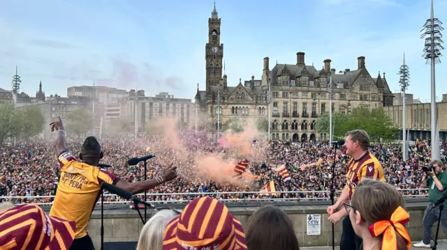 Bantam of the Opera singing in front of thousands of Bradford City fans with orange smoke in the air and City Hall in the background.