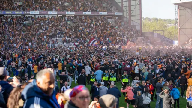 Football fans in stands and on pitch celebrating promotion